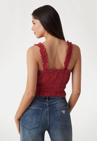 Top court texturé rouge avec des bretelles volantées et un design smocké, associé à un jean en denim bleu avec des poches arrière et un accent de logo.