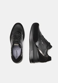 Des sneakers noirs avec une combinaison de cuir lisse et de suède, présentant un design élégant, un bout arrondi et une semelle compensée surélevée.