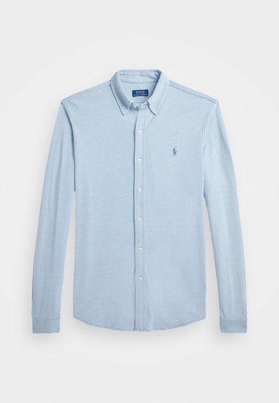 Šviesiai mėlynas ilgomis rankovėmis mygtukais segamas marškinis pagamintas iš medvilnės. Yra mažas išsiuvinėtas logotipas ir klasikinė apykaklė su užsegamomis rankovėmis.