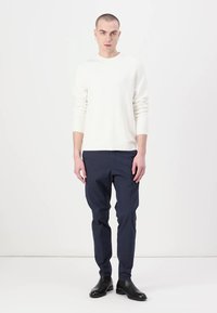 White textured knit sweater, navy trousers with a slim fit, and black leather ankle boots. Model standing against a plain background.