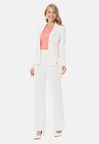 Weißer Blazer mit Reverskragen und zwei Taschen, kombiniert mit passenden weit geschnittenen Hosen; korallenfarbenes, kurzes Oberteil darunter; glattes Material.