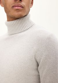 Hellgrauer Rollkragenpullover aus weichem Strickstoff mit geripptem Kragen. Nahaufnahme, die die Textur und das taillierte Design zeigt.