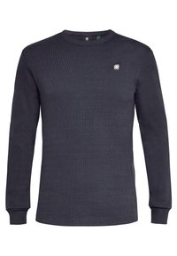 Mörkblå ribbad sweatshirt med lång ärm och rund halsringning, med en liten logotyp på bröstet och åtsittande ärmslut. Tillverkad av mjukt tyg.