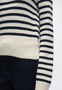 Pull en tricot rayé avec des rayures horizontales alternées noires et blanc cassé, associé à un jean en denim bleu foncé.