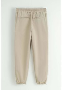 Pantalons beige à taille élastique avec deux poches arrière et des poignets élastiques aux chevilles. Texture lisse et tissu léger.