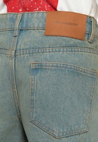 Ανοιχτό μπλε τζιν παντελόνι με υφή, διαθέτει μια καφέ δερμάτινη ετικέτα με την επιγραφή "PESGADOR" στη μέση και μια μόνο πίσω τσέπη.