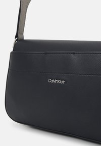 Calvin Klein torba u tamnoplavoj teksturiranoj tkanini s glatkom završnom obradom. Srebrni logo kao dekorativni detalj i kontrastna naramenica.