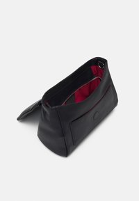 Musta nahkalaukku, jossa on teksturoitu pinta ja punainen sisustus. Varustettu vetoketjulla ja etutaskulla lisäsäilytystä varten.