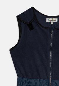 Colete sem mangas azul-marinho com fecho de correr na frente, textura de tecido suave, pescoço com acabamento e uma seção inferior franzida numa tonalidade de azul contrastante.