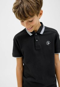 Juodas polo marškinėliai su pilku apykakle ir rankovių akcentais, dviem mygtukais ir apvaliu logotipu kairėje krūtinės pusėje. Minkšta, kvėpuojanti medžiaga.