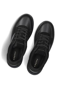 Zwarte sneakers met een leren bovenwerk, textuurdetails, ronde neus en vetersluiting. Logo "Cruyff" zichtbaar op de binnenzool.