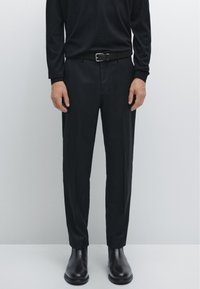 Zwarte lange mouwen shirt, zwarte broek met een riem en zwarte chelsea boots; minimalistisch ontwerp met een zachte textuur en een op maat gemaakte pasvorm.