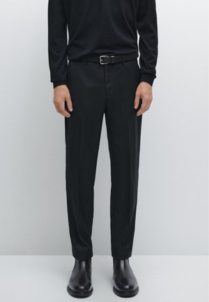 Schwarzes Langarmhemd, schwarze Hose mit einem Gürtel und schwarze Chelsea-Stiefel; minimales Design mit glatter Textur und maßgeschneiderter Passform.