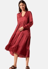 Robe rouge à manches longues avec un décolleté en V et des volants en cascade au bas, fabriquée dans un tissu lisse. Présente une coupe décontractée et un design informel.