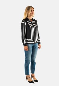Blusa de rayas blancas y negras con cuello, combinada con jeans de mezclilla azul claro. El modelo lleva unos tacones negros con cintas al tobillo.