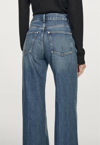 Szerokie niebieskie dżinsy z wysokim stanem, z dwiema tylnymi kieszeniami i widocznymi detalami szwów. Tkanina ma teksturowane wykończenie.