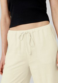 Pantalons amples couleur crème avec une taille élastique et un cordon de serrage. Fabriqués en tissu léger avec une texture subtile.