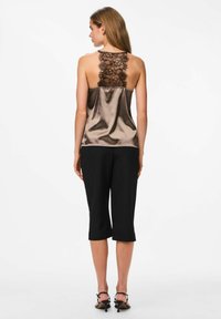 Camisole in satin bronzo con dettagli in pizzo nero sul retro, abbinato a pantaloni cropped neri. Presenta spalline regolabili e una vestibilità rilassata.