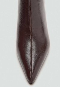 Talons aiguilles en cuir bordeaux à bout pointu avec une texture lisse et des coutures contrastantes le long de la couture centrale.