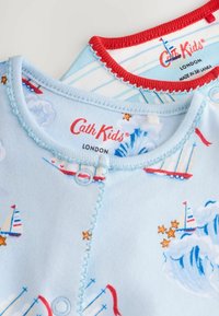 Svetlomodrý bavlnený detský body s pestrým vzorom plachetníc, červeným lemovaním a patentkami. Štítok znie "Cath Kids, Londýn."