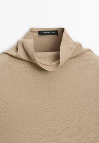 Beżowa, prążkowana bluzka z długim rękawem i golfem, charakteryzująca się miękką teksturą i prostym wzornictwem. Metka głosi "Massimo Dutti, wyprodukowano w Chinach."