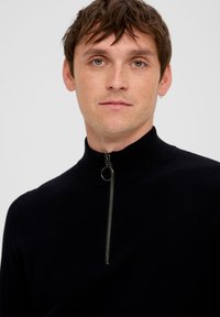 Czarny dziany sweter z wysokim kołnierzem i półzamkiem z przodu. Posiada teksturowany materiał oraz dekoracyjny metalowy suwak.
