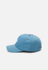 Blå bomullslue med buet skjerm, seks ventilasjonshull og en brodert logo foran. Har en justerbar stropp bak.