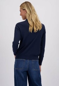 Navyblauwe trui met lange mouwen, geribbelde zoom en een klassieke pasvorm, gecombineerd met hoogontwikkelde donkerdenim jeans met achterzakken.