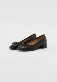 Ballet flats in pelle nera con punta arrotondata, piccolo tacco a blocco e decorazione a fiocco sul frontale. Texture liscia e design minimalista.