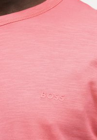 Κοντινό πλάνο ενός ατόμου που φοράει ένα ροζ υφασμάτινο T-shirt με τη λέξη «BOSS» ανάγλυφα στο στήθος.