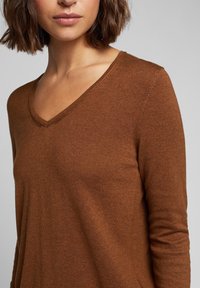 Brązowy sweter dzianinowy z dekoltem w kształcie litery V, długimi rękawami i miękką fakturą. Posiada minimalne przeszycia i dopasowany krój.