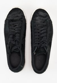 Baskets noires avec une texture ressemblant à de la fourrure sur le dessus, un design à lacets et des semelles en caoutchouc blanches. Accents noirs mats et lisses partout.