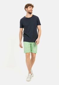 Mannen navy t-shirt in combinatie met lichtgroene shorts, met een relaxte pasvorm. Witte sneakers maken de casual look compleet.