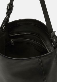 Czarna skórzana torebka o miękkiej fakturze, z wewnętrzną kieszenią na suwak i gładkim wykończeniem. Pasek jest regulowany, co zapewnia wszechstronność.