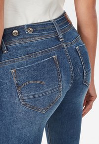 Jeans in denim con vita alta, colore blu, cuciture a contrasto e due tasche posteriori con design curvi.