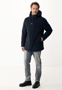 Veste à capuche navy avec fermeture éclair à l'avant et fermoir à pression, dotée de deux poches latérales et d'un tissu lisse et durable. Associée à un jean gris et des bottes noires.