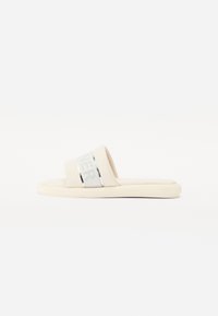 Sandales à glissière beige avec une large sangle ornée d'accents argentés et du mot "RUNNER". Semelle douce et rembourrée pour le confort. Texture lisse.