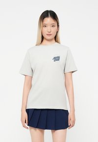 Tricou din bumbac gri deschis, cu guler rotund, mâneci scurte și un grafic al logo-ului "Santa Cruz" de culoare albastră pe partea stângă a pieptului.