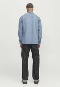 Giacca di jeans azzurro chiaro con maniche lunghe, dettagli con yoke sul retro e polsini con bottoni, abbinata a jeans di denim scuro e stivali marroni.