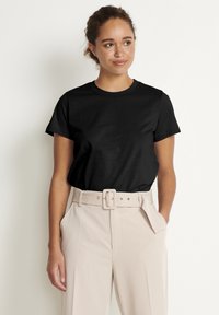 Black cotton t-shirt with short sleeves and a crew neckline, paired with high-waisted beige trousers featuring a wide belt and belt loops.