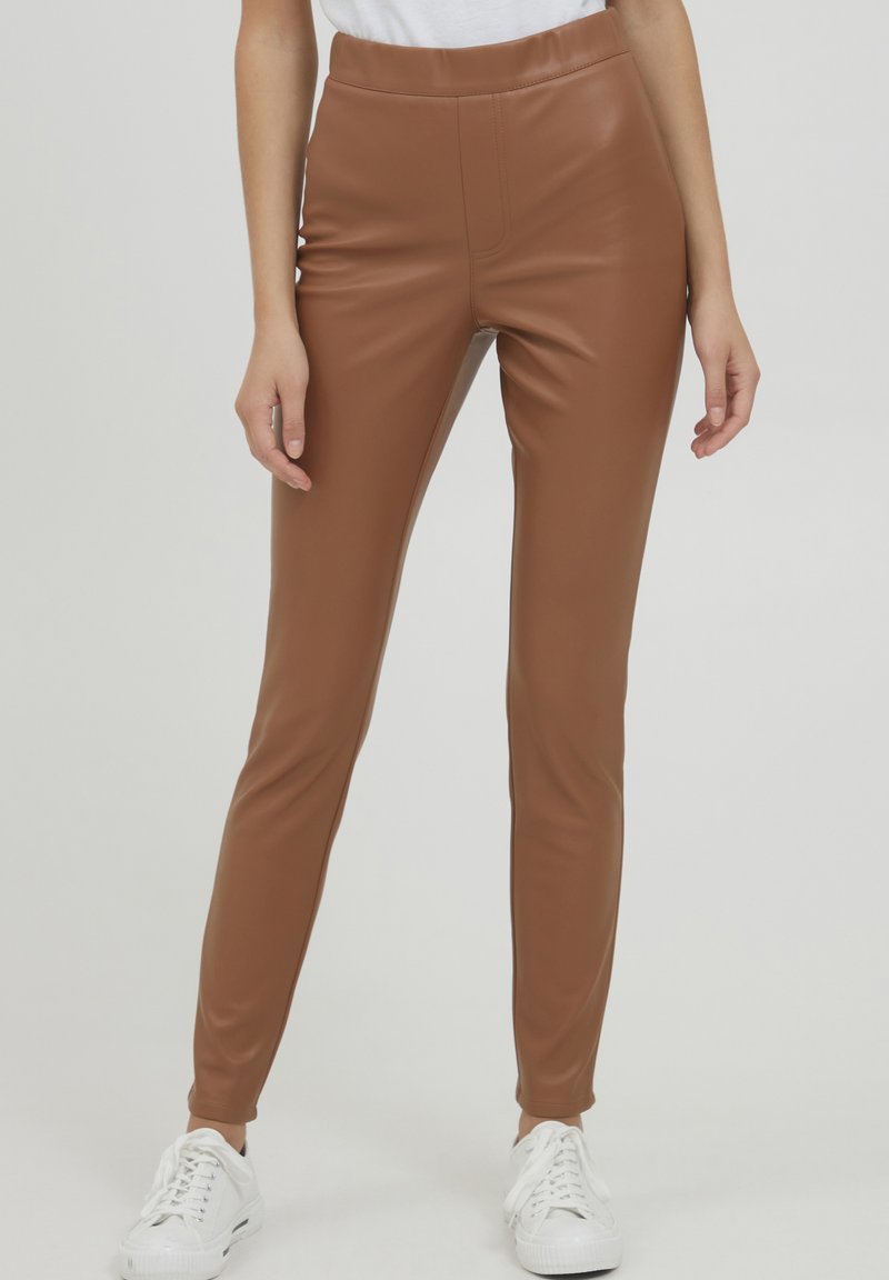 Bruine neplederen leggings met een gladde textuur, hoge tailleband en slim fit, gecombineerd met witte sneakers. Geen zichtbare patronen of accenten.