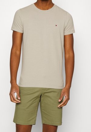 T-shirt in cotone beige con maniche corte e scollatura tonda, caratterizzato da un piccolo logo rosso e blu sul petto, abbinato a pantaloni corti verde oliva.