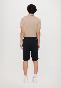 Beige polos tričko s krátkým rukávem, námořnické šortky a bílé tenisky. Šortky mají elastický pas a detail kapsy na zadní straně.