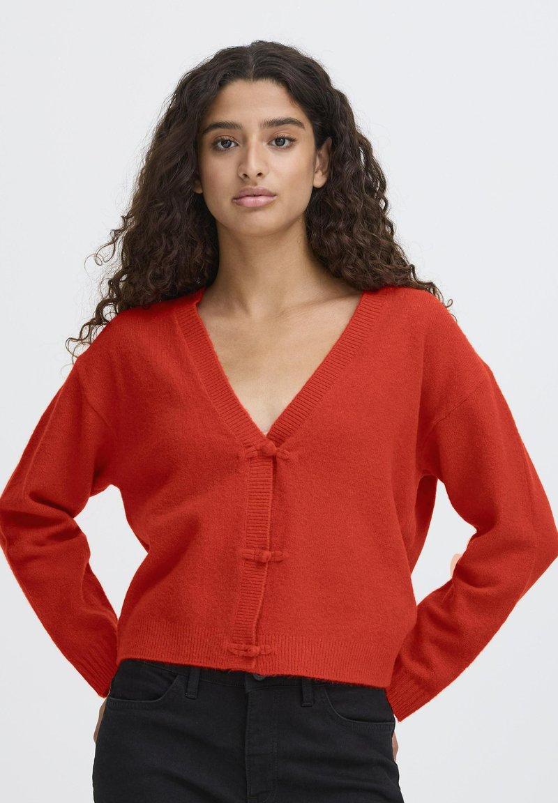 Cardigan rosso a maglia con scollatura a V, caratterizzato da una vestibilità cropped, maniche lunghe e chiusura con bottoni a toggle davanti. Texture morbida in tutto il capo.