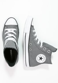 Sneaker alte bianche e nere con un motivo testurizzato, lacci bianchi e una toppa rotonda con logo sul lato. Suola in gomma e punta rinforzata.