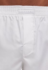 Shorts de bain blancs avec une ceinture élastique, comprenant une petite poche arrière, une texture en chevrons et une étiquette visible portant l'inscription "FALKE".