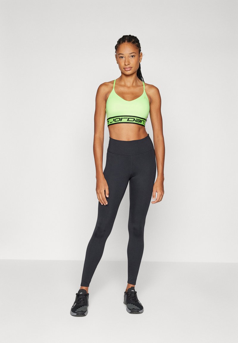 Conjunto deportivo que incluye un sujetador deportivo de color verde neón con banda negra con logo y leggings negros de cintura alta. Tejido texturizado y diseño ajustado.
