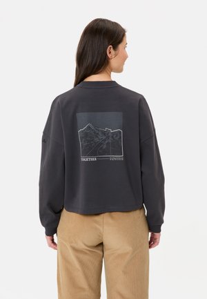 Korte grijze sweatshirt van zachte stof, met een bergafbeelding op de achterkant en het woord "SAMEN" eronder.