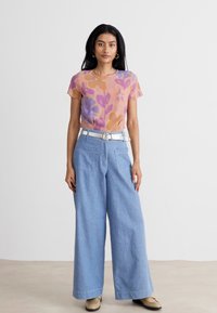 Floral-patterned sheer top in pastel colors, paired with light blue wide-leg denim pants. Complete with a white belt and beige shoes.