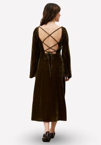 Robe longue en velours vert olive avec manches longues, dos ouvert avec des bretelles croisées et une fermeture à nouer à la taille. Design classique.